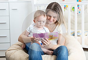 Portrait of beautiful mother holding baby on her lap and reading