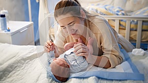 Portrait of beautiful mother holding hands of her little baby son lying on bed at night