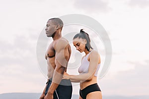 Portrait of beautiful muscular mixed race couple with perfect bodies in sportswear softly embracing on mountains