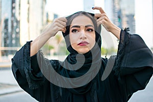 Portrait of beautiful muslim woman fixing headscarf abaya on the street.