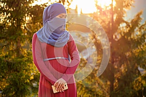 Portrait of beautiful Muslim woman with green eyes wearing blue scarf face closed covered with aveil background forest