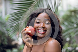Portrait of beautiful naked young african girl with a light natural make-up and perfect skin with pomegranate in her