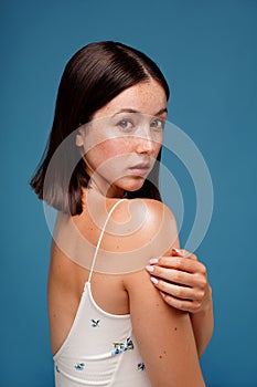 Portrait of beautiful natural woman looking camera, posing on the blue studio background. Girl with freckles