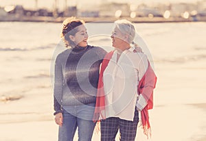 Portrait of beautiful older mom and mature daughter walking on the beach at autumn sunset