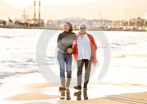 Portrait of beautiful older mom and mature daughter walking on the beach at autumn sunset