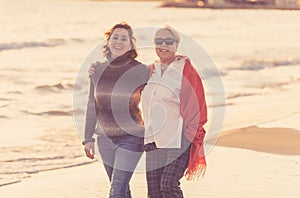 Portrait of beautiful older mom and mature daughter walking on the beach at autumn sunset