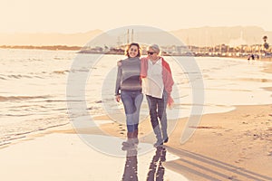 Portrait of beautiful older mom and mature daughter walking on the beach at autumn sunset