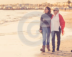 Portrait of beautiful older mom and mature daughter walking on the beach at autumn sunset