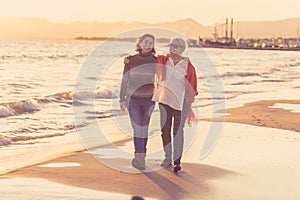 Portrait of beautiful older mom and mature daughter walking on the beach at autumn sunset