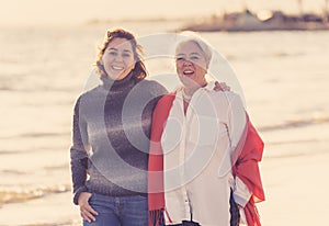 Portrait of beautiful older mom and mature daughter walking on the beach at autumn sunset