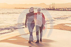 Portrait of beautiful older mom and mature daughter walking on the beach at autumn sunset