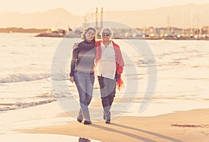 Portrait of beautiful older mom and mature daughter walking on the beach at autumn sunset