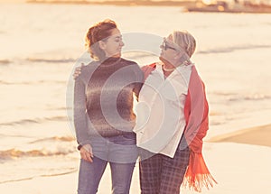 Portrait of beautiful older mom and mature daughter walking on the beach at autumn sunset