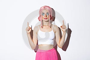 Portrait of beautiful party girl with pink wig and glamour makeup, pointing fingers and looking up, showing your logo