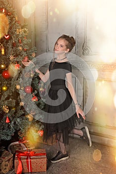 Portrait of a beautiful pensive girl in black near the Christmas tree at Christmas