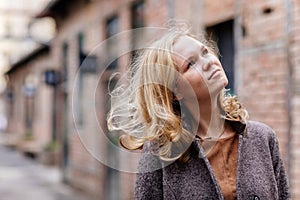 Portrait of beautiful pensive woman grins, eyes glistening, young Caucasian female person, blonde girl looking away, gray coat and