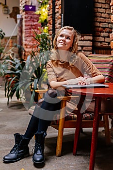 Portrait of beautiful pensive woman grins, eyes glistening, young Caucasian female person at cafe, blonde girl looking away, beige