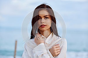 Portrait of a beautiful pensive woman with tanned skin in a white beach shirt with wet hair after swimming on the beach