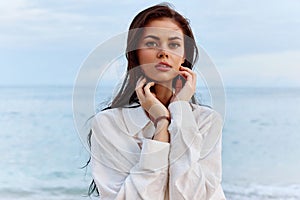 Portrait of a beautiful pensive woman with tanned skin in a white beach shirt with wet hair after swimming on the beach