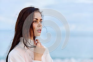 Portrait of a beautiful pensive woman with tanned skin in a white beach shirt with wet hair after swimming on the beach