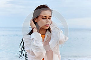 Portrait of a beautiful pensive woman with tanned skin in a white beach shirt with wet hair after swimming on the beach