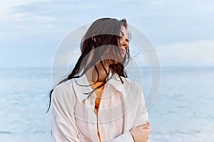 Portrait of a beautiful pensive woman with tanned skin in a white beach shirt with wet hair after swimming on the beach