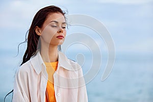 Portrait of a beautiful pensive woman with tanned skin in a white beach shirt with wet hair after swimming on the beach