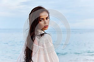 Portrait of a beautiful pensive woman with tanned skin in a white beach shirt with wet hair after swimming on the beach