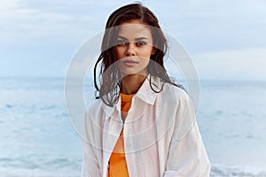 Portrait of a beautiful pensive woman with tanned skin in a white beach shirt with wet hair after swimming on the beach