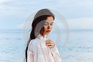 Portrait of a beautiful pensive woman with tanned skin in a white beach shirt with wet hair after swimming on the ocean