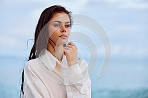 Portrait of a beautiful pensive woman with tanned skin in a white beach shirt with wet hair after swimming on the ocean