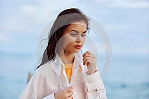 Portrait of a beautiful pensive woman with tanned skin in a white beach shirt with wet hair after swimming on the ocean