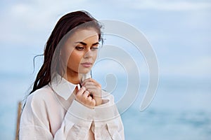 Portrait of a beautiful pensive woman with tanned skin in a white beach shirt with wet hair after swimming on the ocean