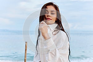 Portrait of a beautiful pensive woman with tanned skin in a white beach shirt with wet hair after swimming on the ocean