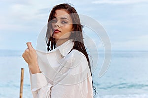 Portrait of a beautiful pensive woman with tanned skin in a white beach shirt with wet hair after swimming on the ocean