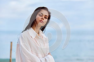 Portrait of a beautiful pensive woman with tanned skin in a white beach shirt with wet hair after swimming on the ocean