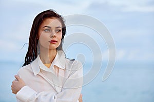 Portrait of a beautiful pensive woman with tanned skin in a white beach shirt with wet hair after swimming on the ocean