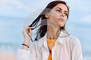 Portrait of a beautiful pensive woman with tanned skin in a yellow tank top and white beach shirt with wet hair after