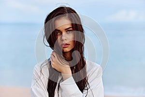 Portrait of a beautiful pensive woman with tanned skin in a yellow tank top and white beach shirt with wet hair after