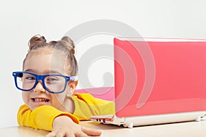 Portrait of beautiful playful little girl with glasses using laptop computer