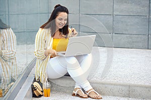 Portrait of beautiful plus size woman 30-35 years old in fashion clothes and eyeglasses working remotely on a laptop