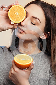 Portrait of a beautiful positive girl with long hair and orange, a young woman smiling and holding fruit near face on studio