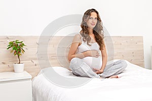 Portrait of a beautiful pregnant long haired woman sitting on the sofa, smiling and looking at camera.