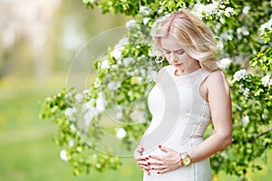 Portrait of beautiful pregnant woman in the flowering park. Young happy pregnant woman enjoying life in nature