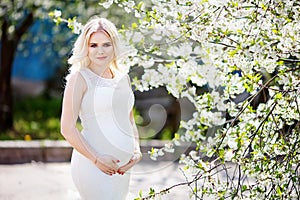 Portrait of beautiful pregnant woman in the flowering park. Young happy pregnant woman enjoying life in nature