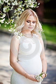 Portrait of beautiful pregnant woman in the flowering park. Young happy pregnant woman enjoying life in nature