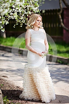 Portrait of beautiful pregnant woman in the flowering park. Young happy pregnant woman enjoying life in nature