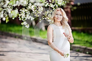 Portrait of beautiful pregnant woman in the flowering park. Young happy pregnant woman enjoying life in nature