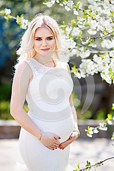 Portrait of beautiful pregnant woman in the flowering park. Young happy pregnant woman enjoying life in nature