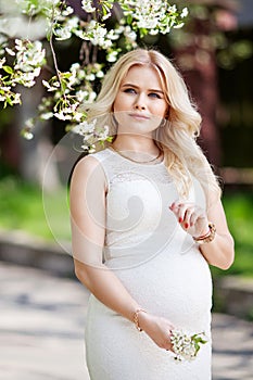Portrait of beautiful pregnant woman in the flowering park. Young happy pregnant woman enjoying life in nature